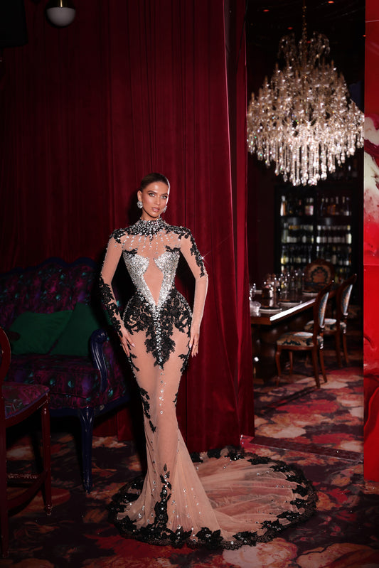 Woman in a glamorous dress standing in an elegant room with red curtains and a chandelier.