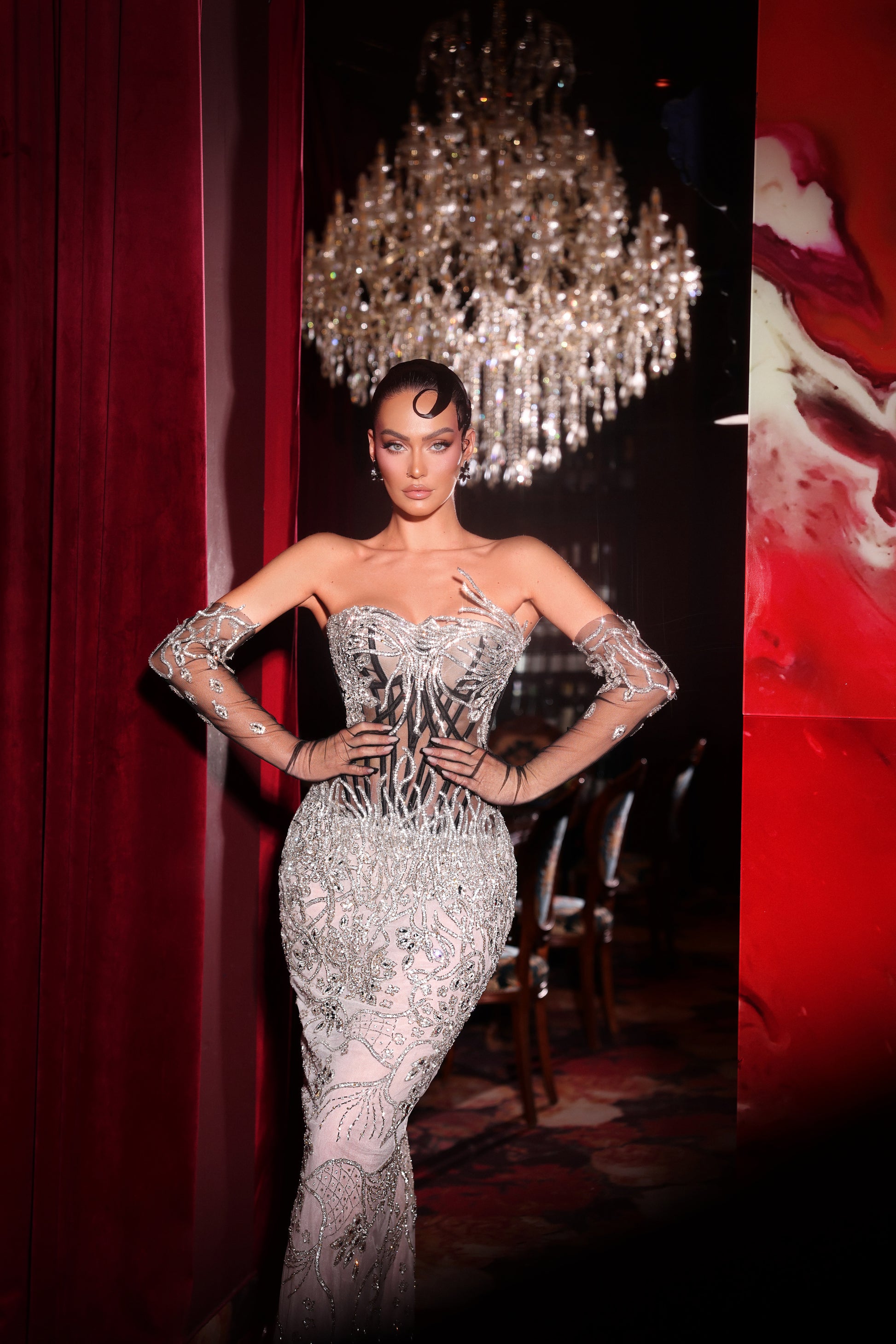 Woman in a sparkling silver dress posing in front of a chandelier