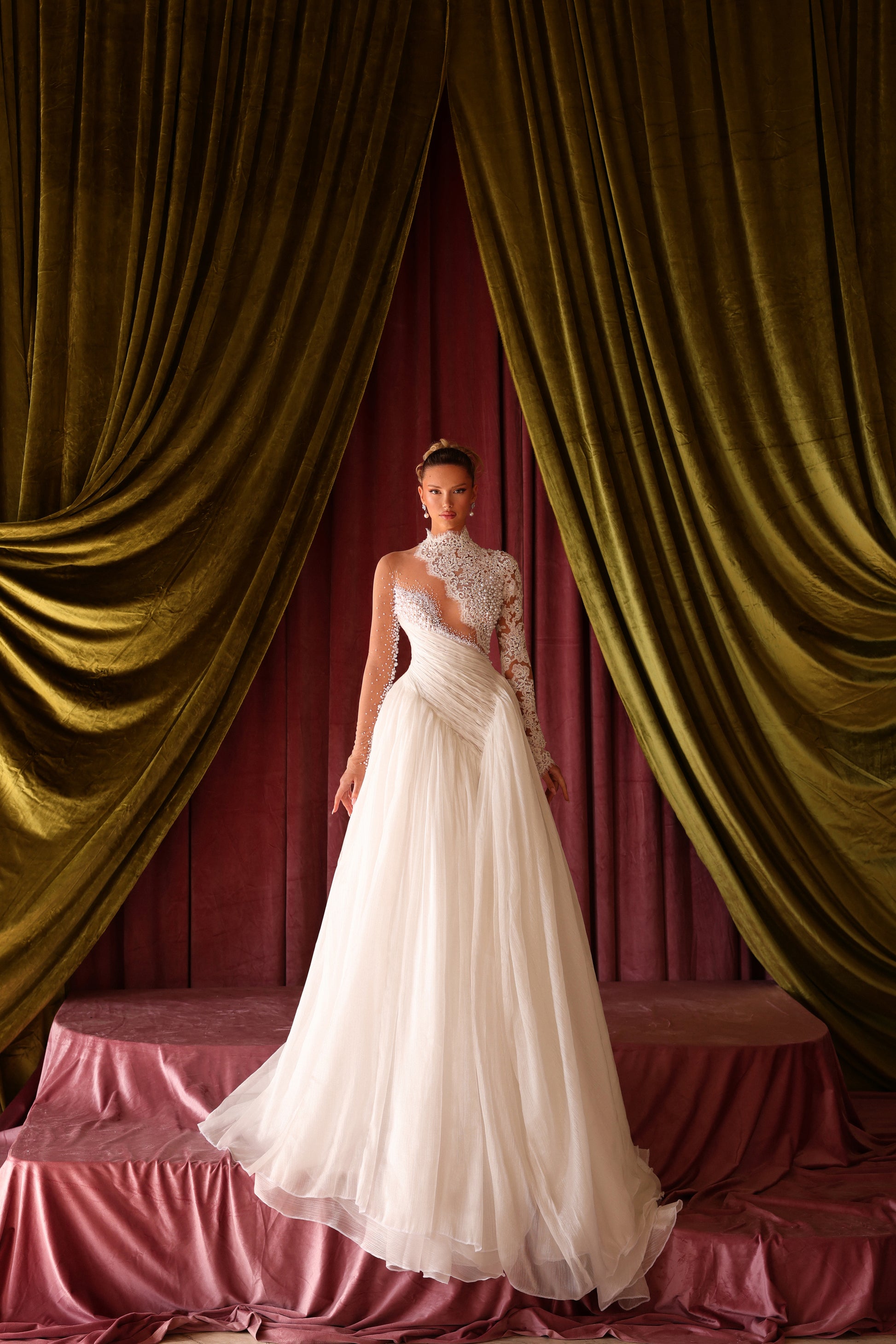 Woman in a white wedding dress standing in front of gold curtains and a red wall.