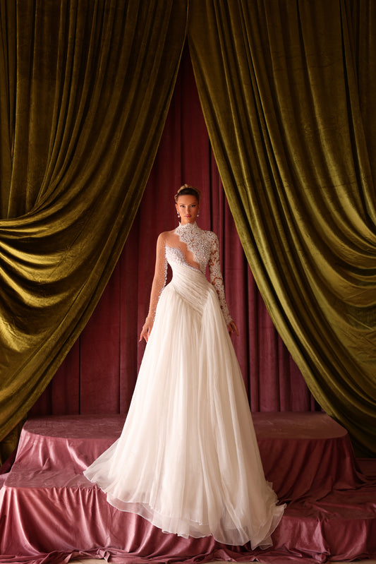 Woman in a white wedding dress standing in front of gold curtains and a red wall.
