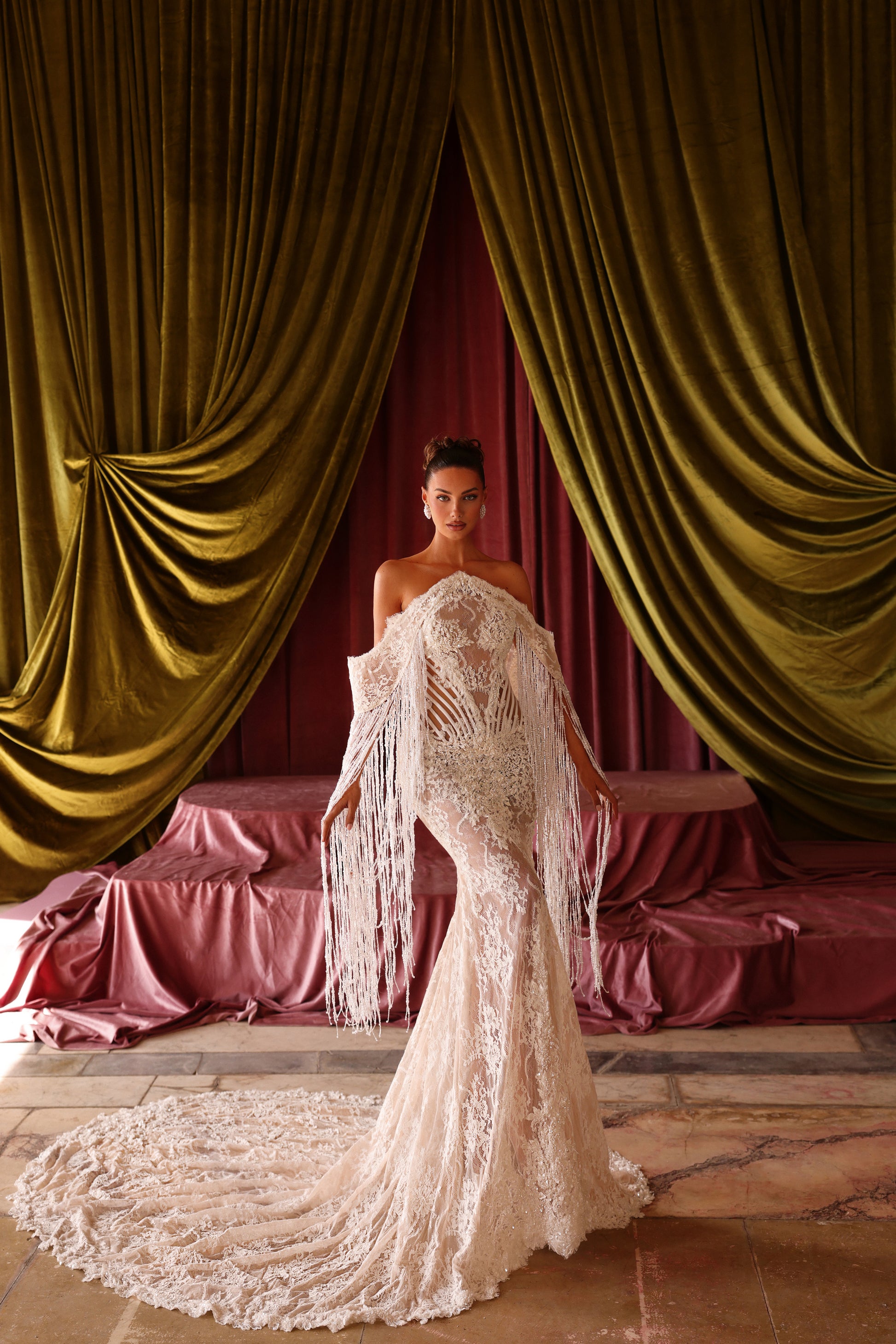 Woman in a white lace dress standing in front of gold curtains