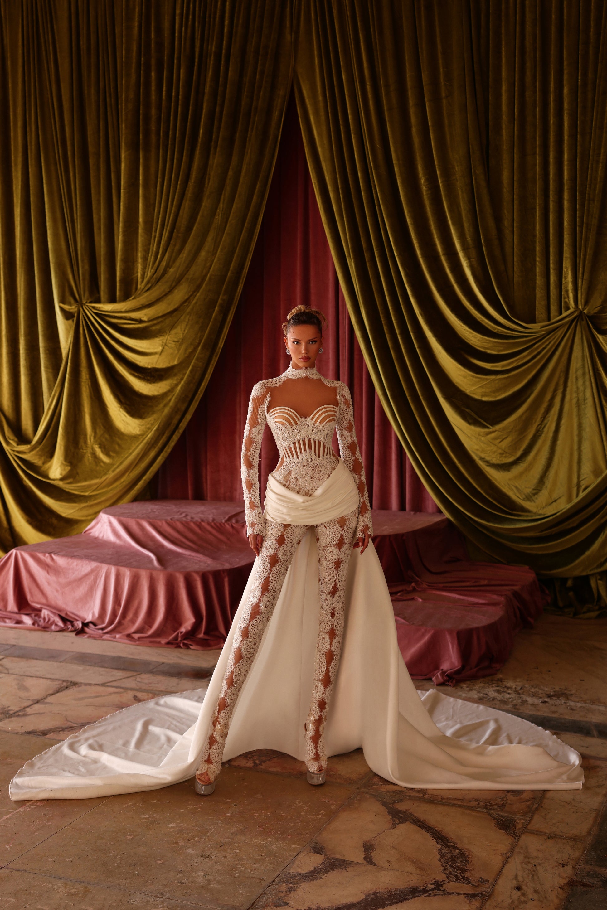 Woman in a white and red floral dress standing in front of gold curtains.