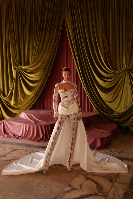 Woman in a white and red floral dress standing in front of gold curtains.