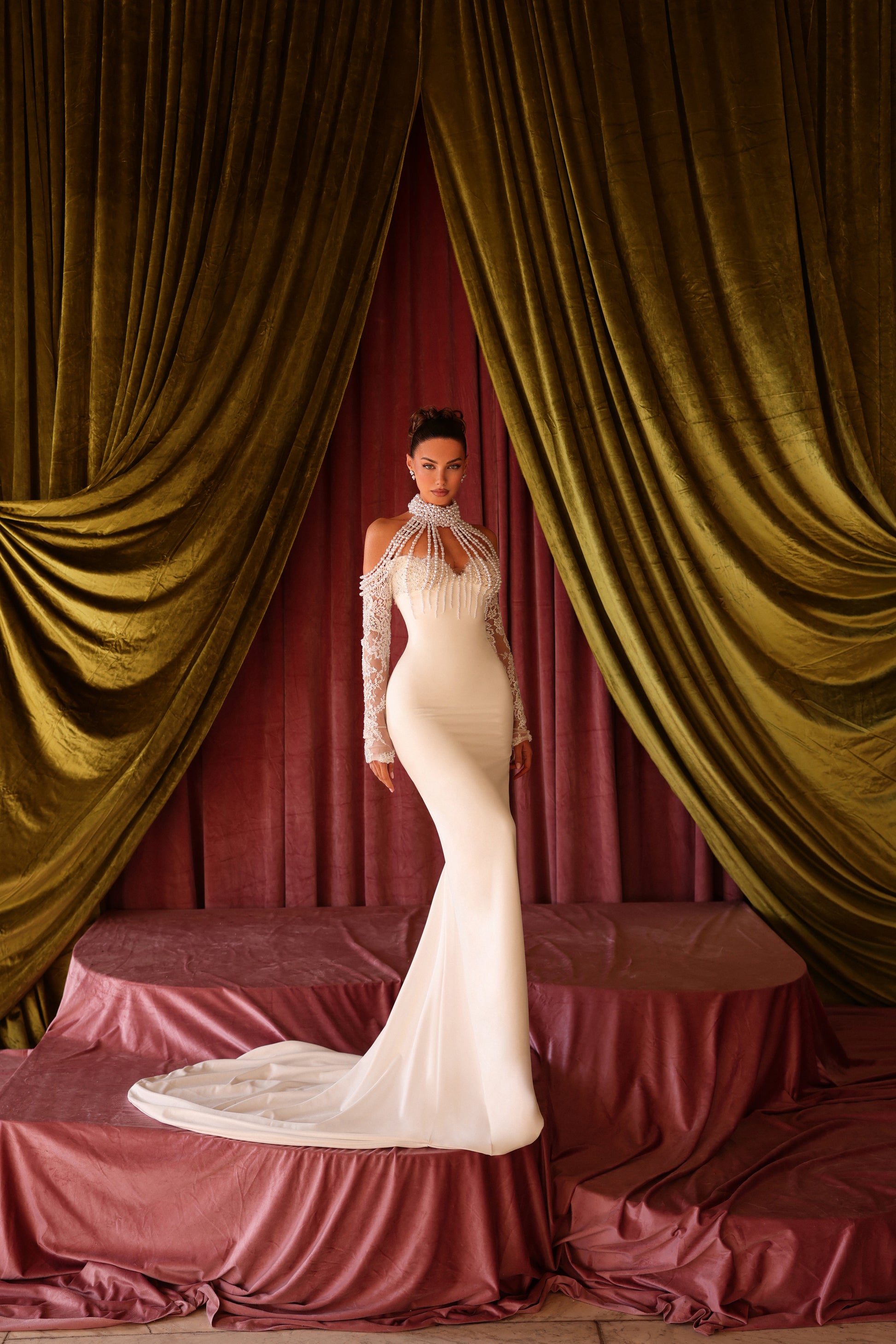 Woman in a white dress standing between gold curtains in a theatrical setting