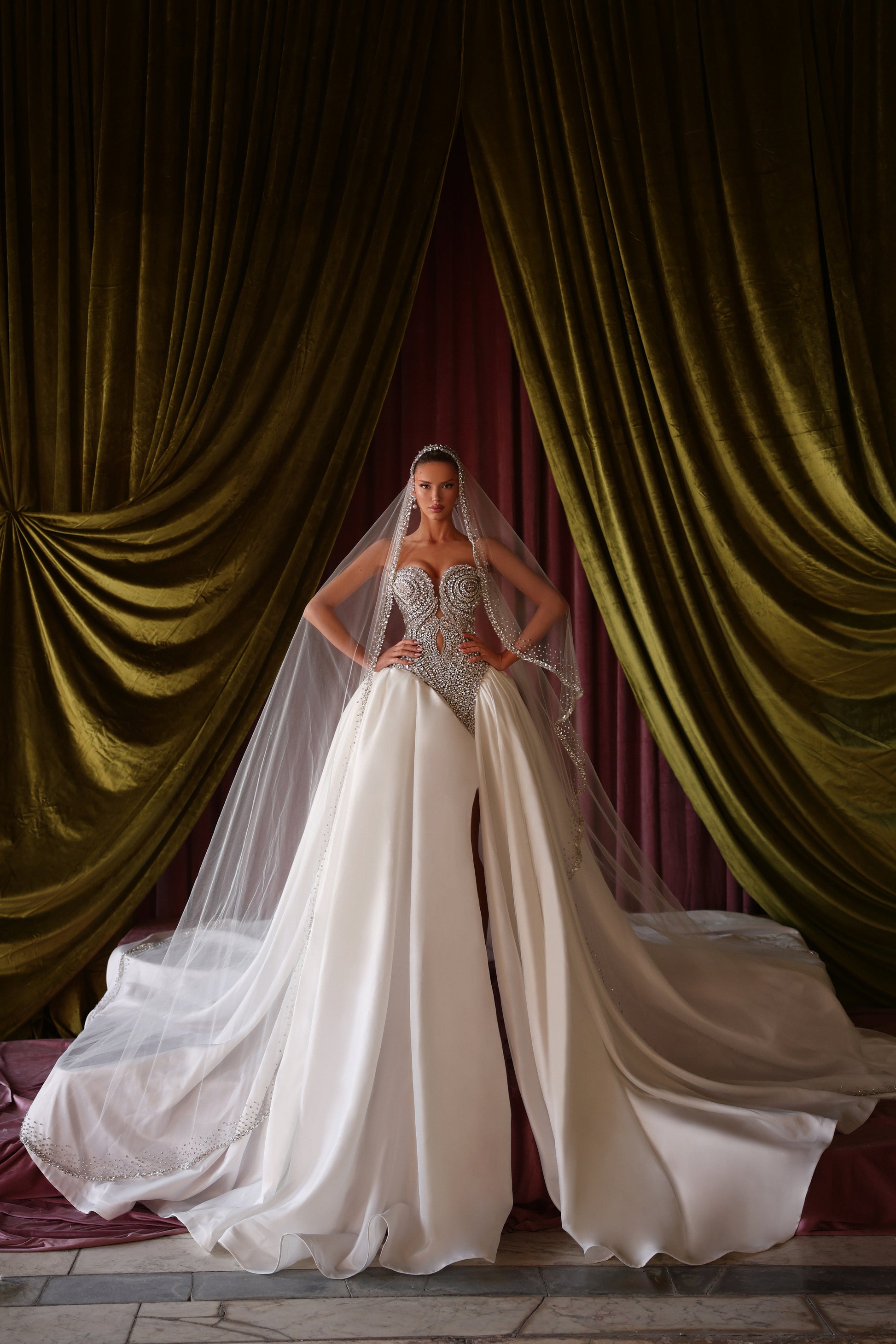 Bride in a white wedding dress with a long train standing in front of green curtains.