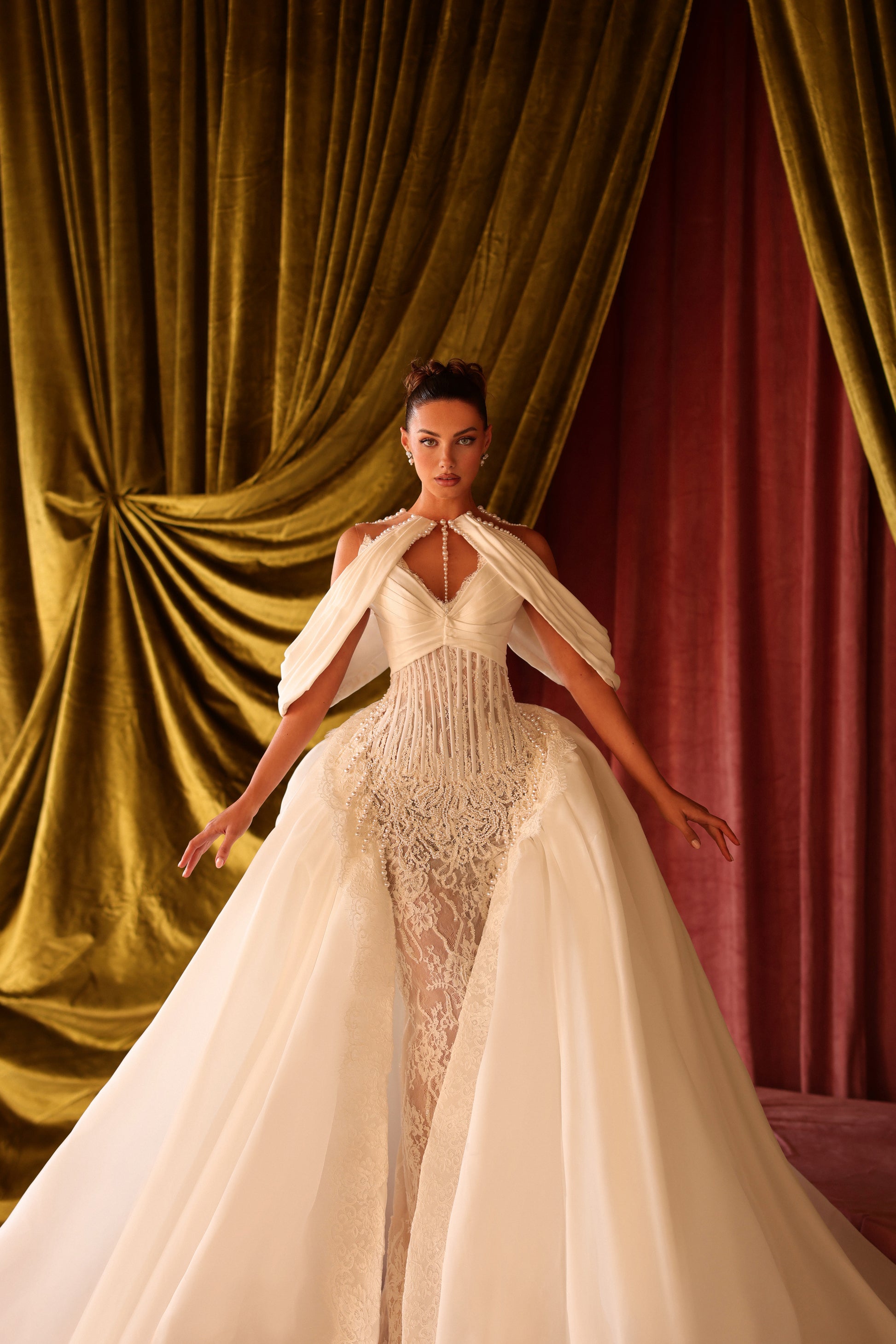 Woman in a white wedding dress standing in front of red and gold draped curtains