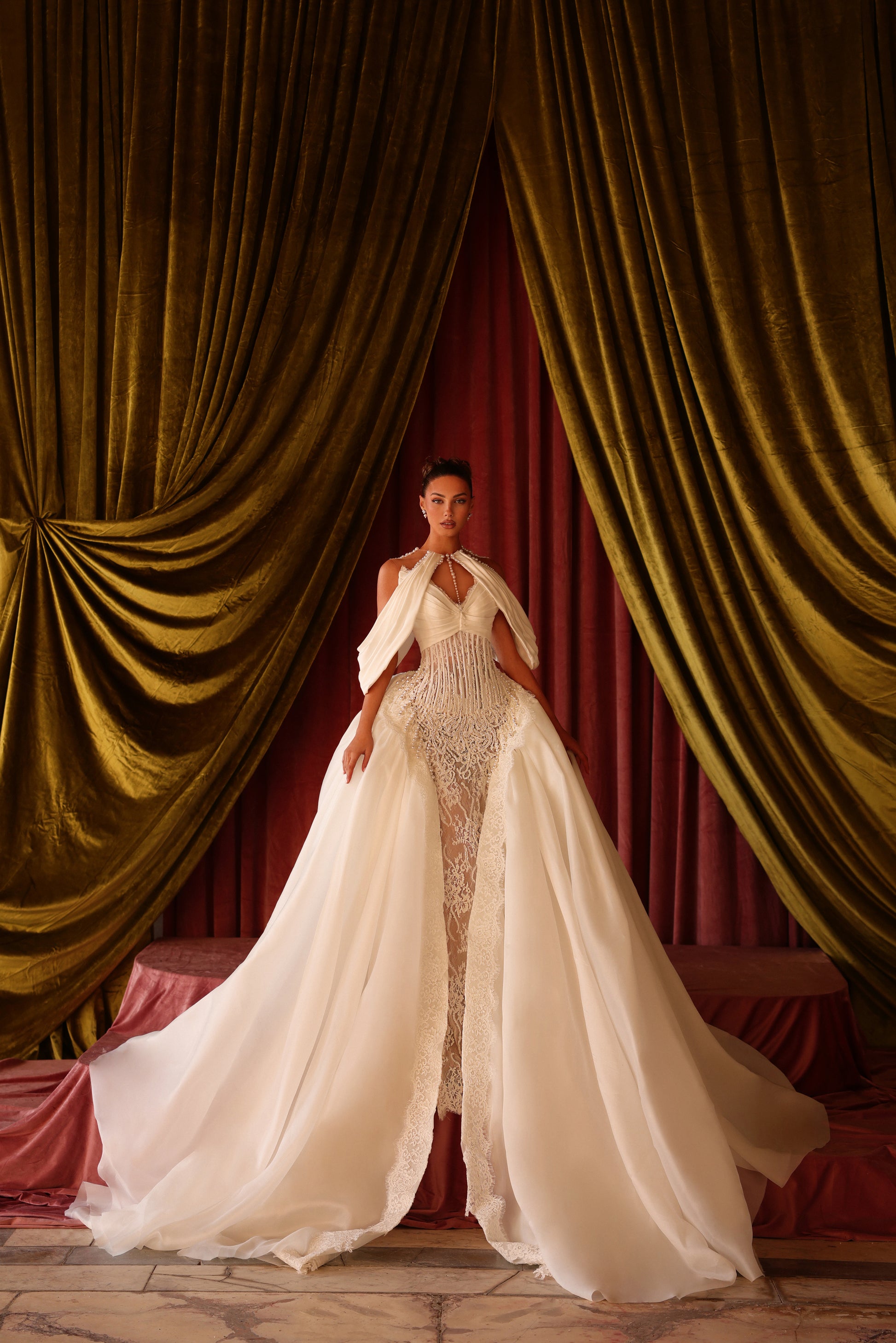 Woman in a white gown standing in front of gold curtains