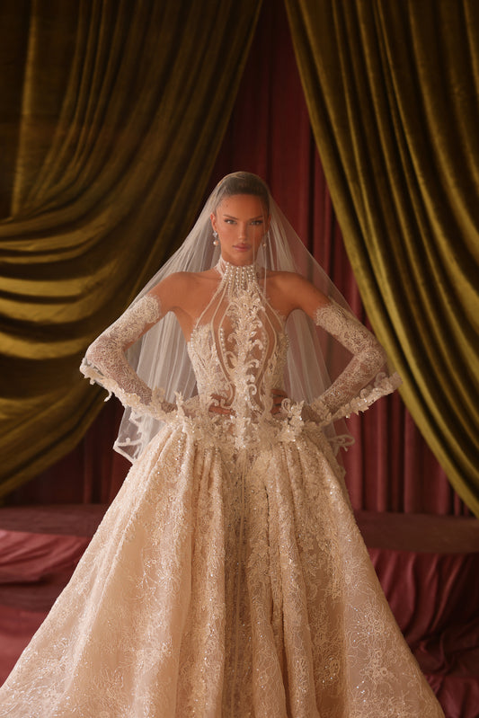 Woman in an elaborate wedding gown with a long veil against a draped curtain background