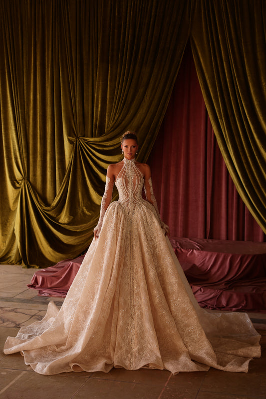 Woman in a beige wedding dress standing in front of ornate gold and red curtains.