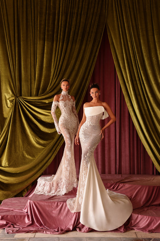 Two models in elegant dresses standing in front of draped curtains.