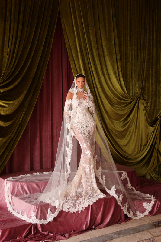 Woman in a white wedding dress with a long veil standing in front of green and red curtains.