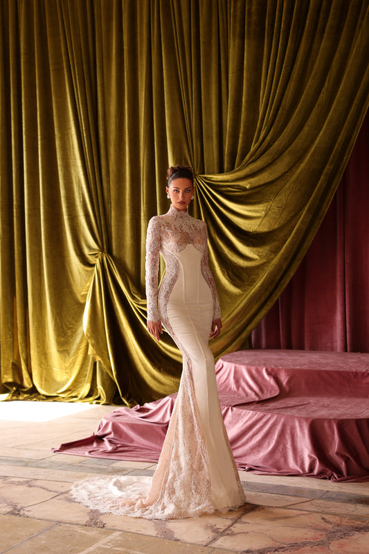 Woman in a white lace dress standing in front of gold and red curtains.