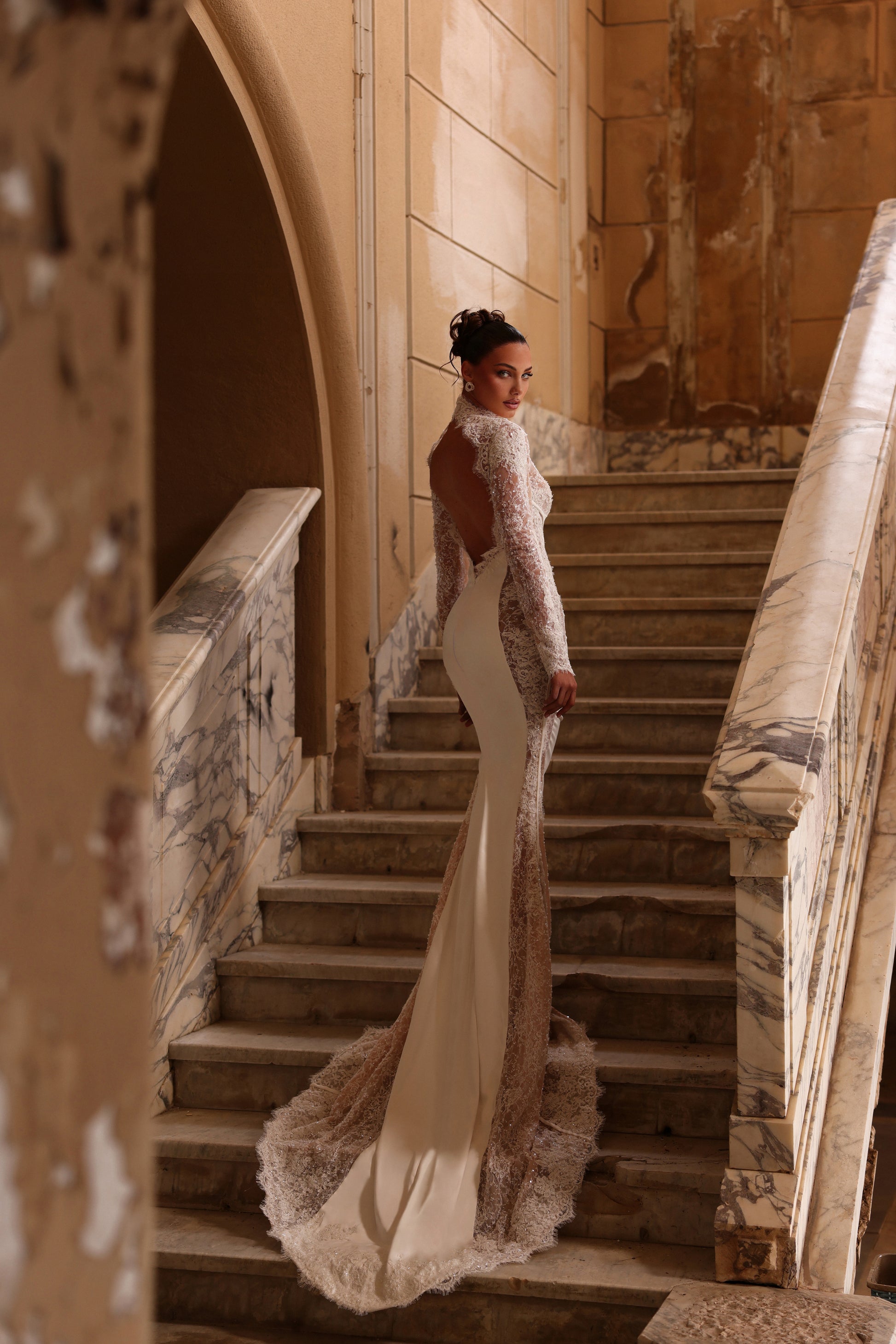 Woman in a white lace gown standing on a marble staircase