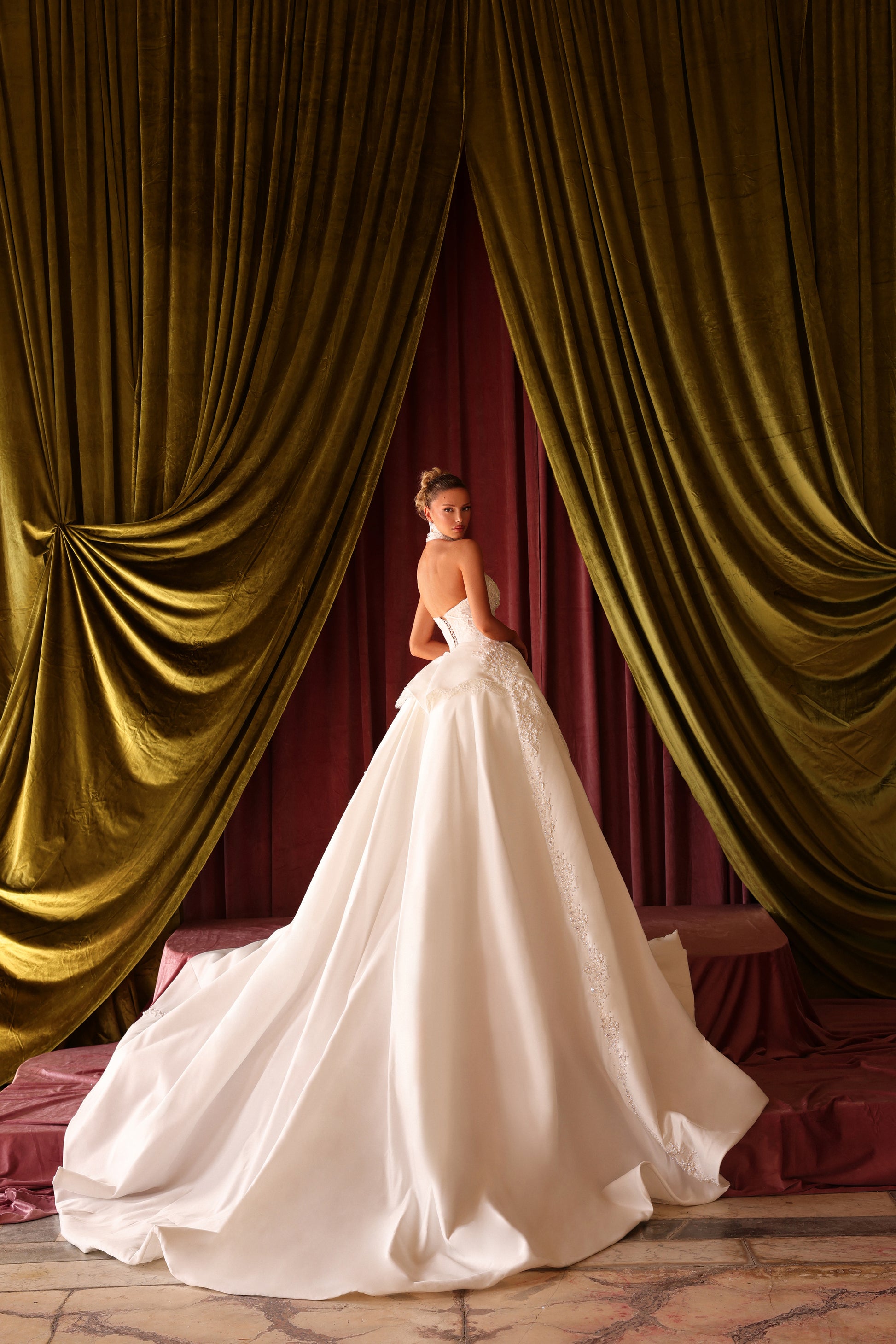 Woman in a white wedding dress standing in front of gold curtains