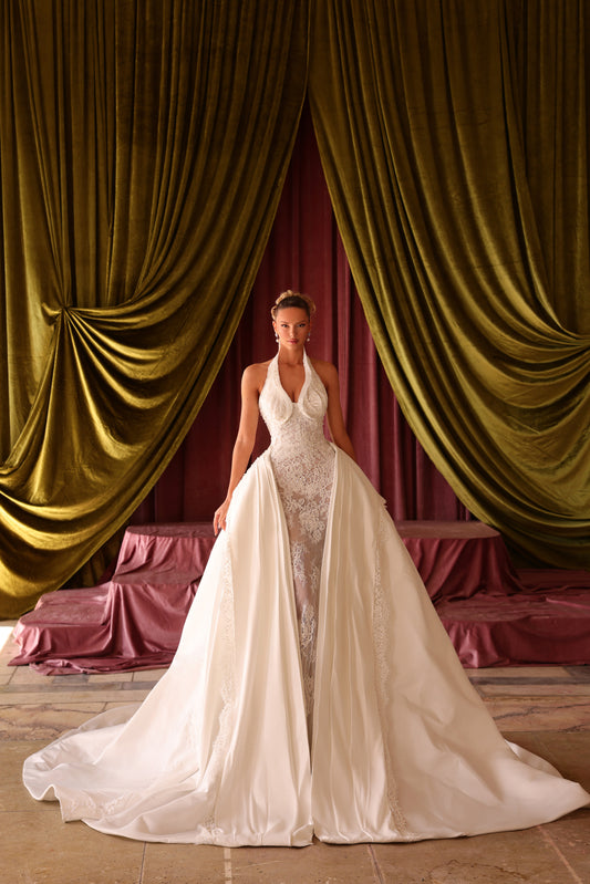 Woman in a white wedding dress standing in front of gold and red draped curtains.