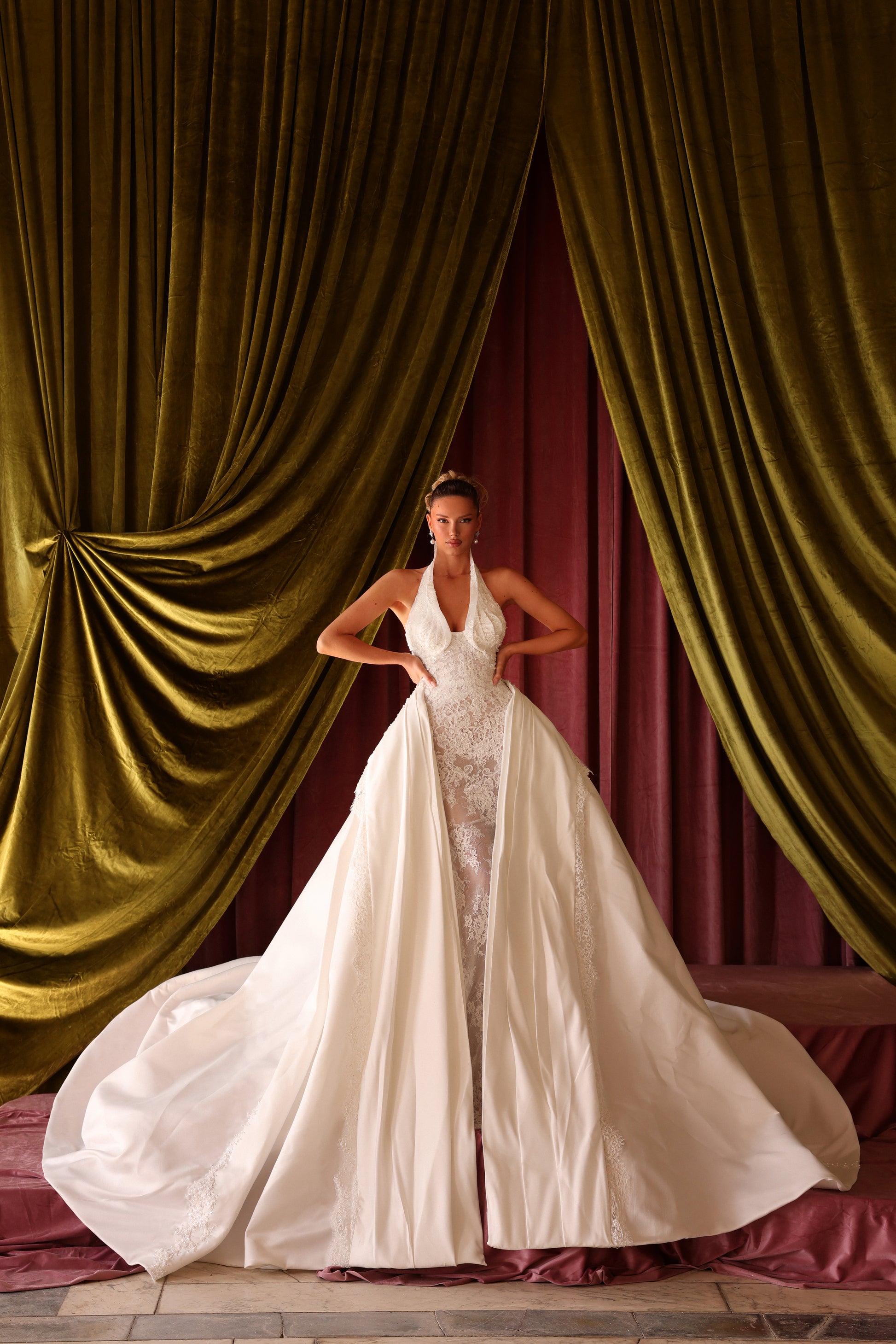 Woman in a white wedding dress standing in front of green and red draped curtains.